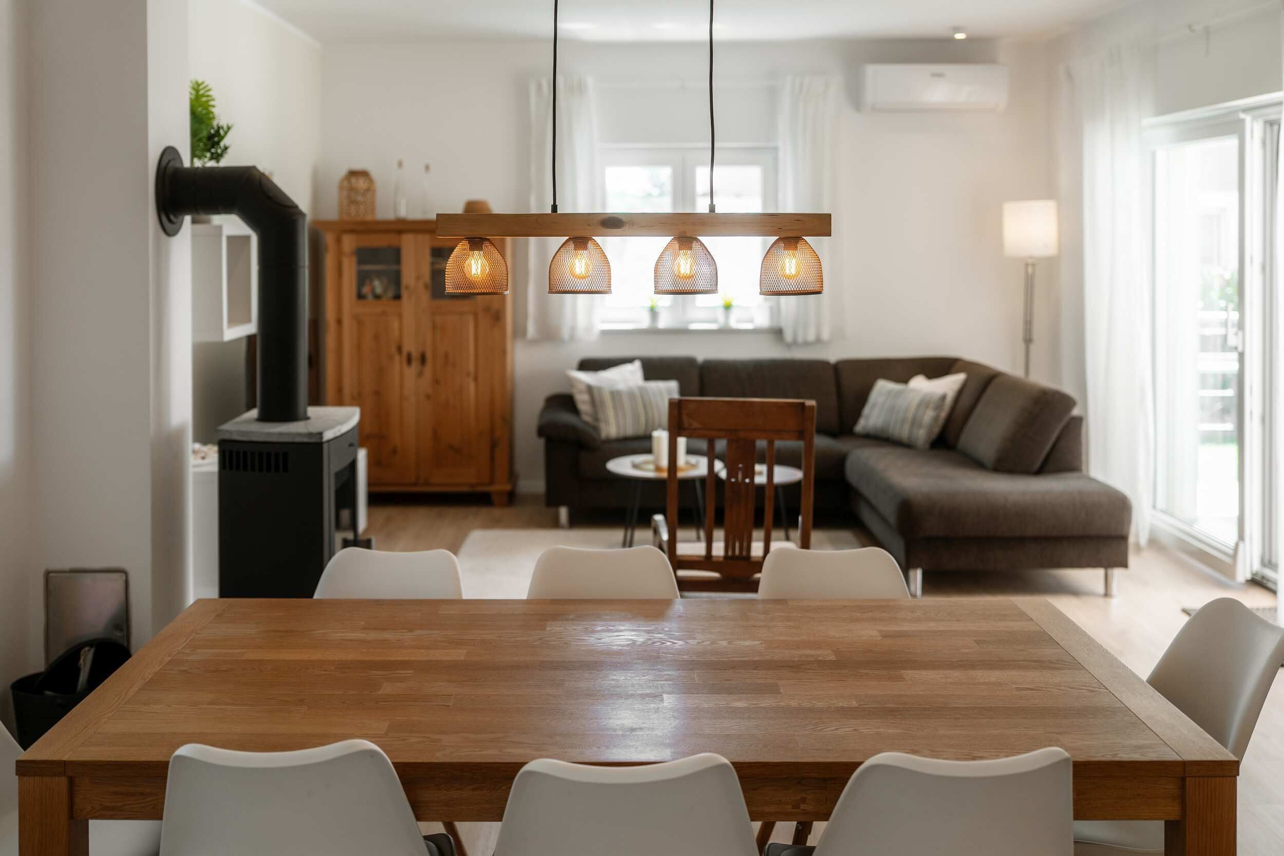 Ein Essbereich mit Holztisch und weißen Stühlen, eine Küche mit Herd und ein Wohnzimmer mit Sofa und Couchtisch.