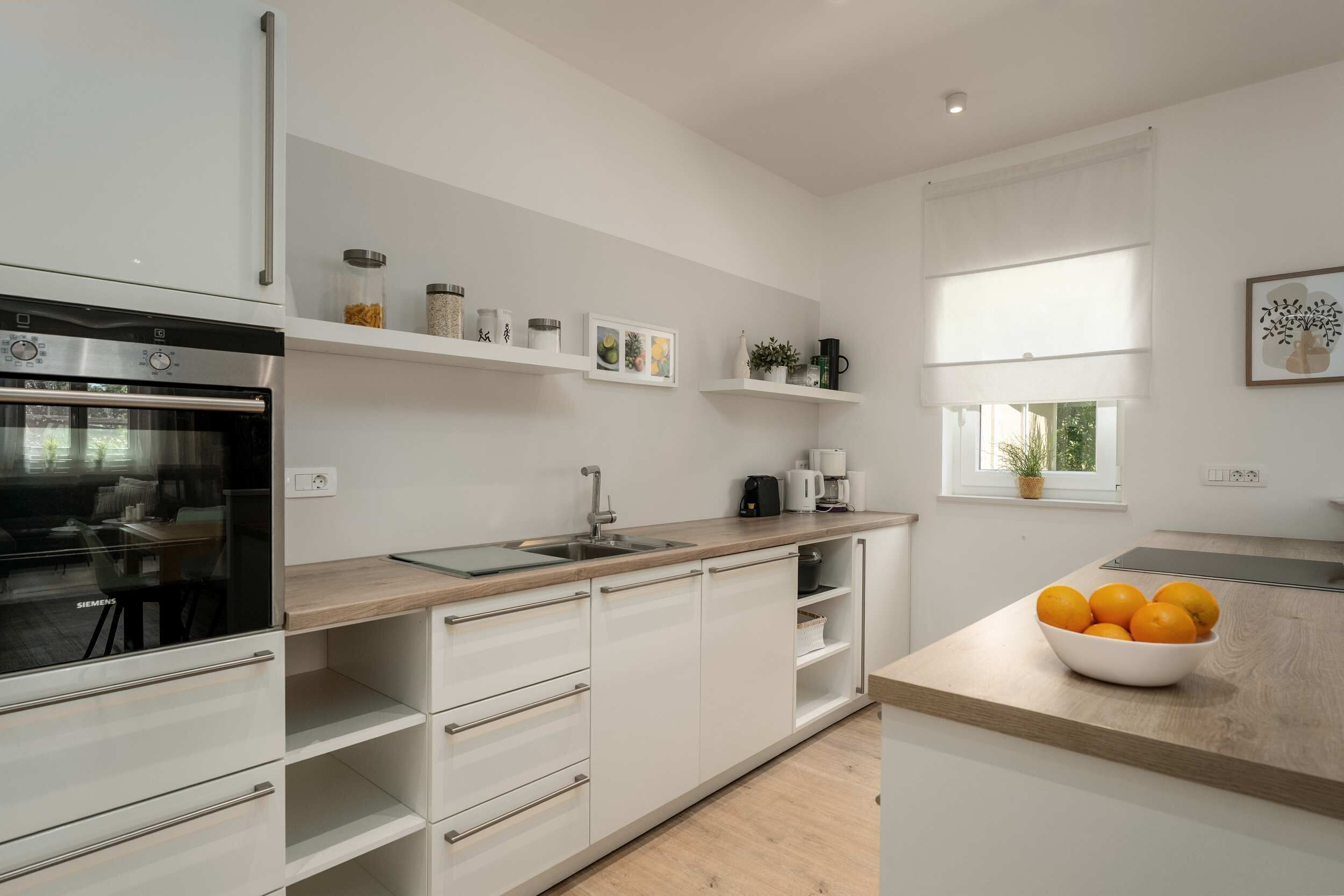 Eine moderne Küche mit weißen Schränken, einem eingebauten Backofen und einem Fenster mit Blick.