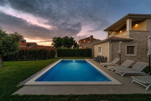 Una piscina rectangular amb gandules i un edifici de pedra amb un balcó.