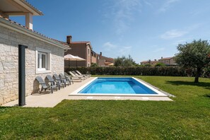 Una piscina con lettini, un edificio in pietra e cielo sereno.