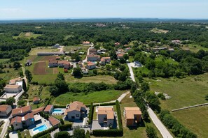 Een luchtfoto van een woongebied met huizen, een zwembad en groene velden.