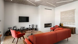 Ein modernes Wohnzimmer mit einer Couch, Sesseln, einem Kamin, einem Fernseher und einer Wanddekoration aus Makramee.