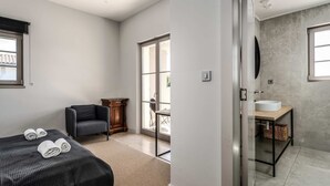 Ein Hotelzimmer mit Bett, Stuhl, kleinem Tisch, Badezimmer mit Waschbecken und großem Fenster.