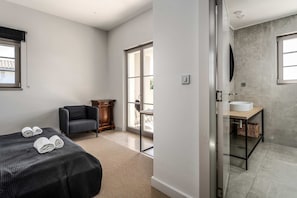 Ein Hotelzimmer mit Bett, Stuhl, kleinem Tisch, Badezimmer mit Waschbecken und großem Fenster.