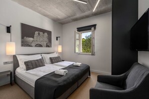 Een moderne hotelkamer met een groot bed, een stoel, een schilderij van een kasteel, een raam met uitzicht en een flatscreen televisie.