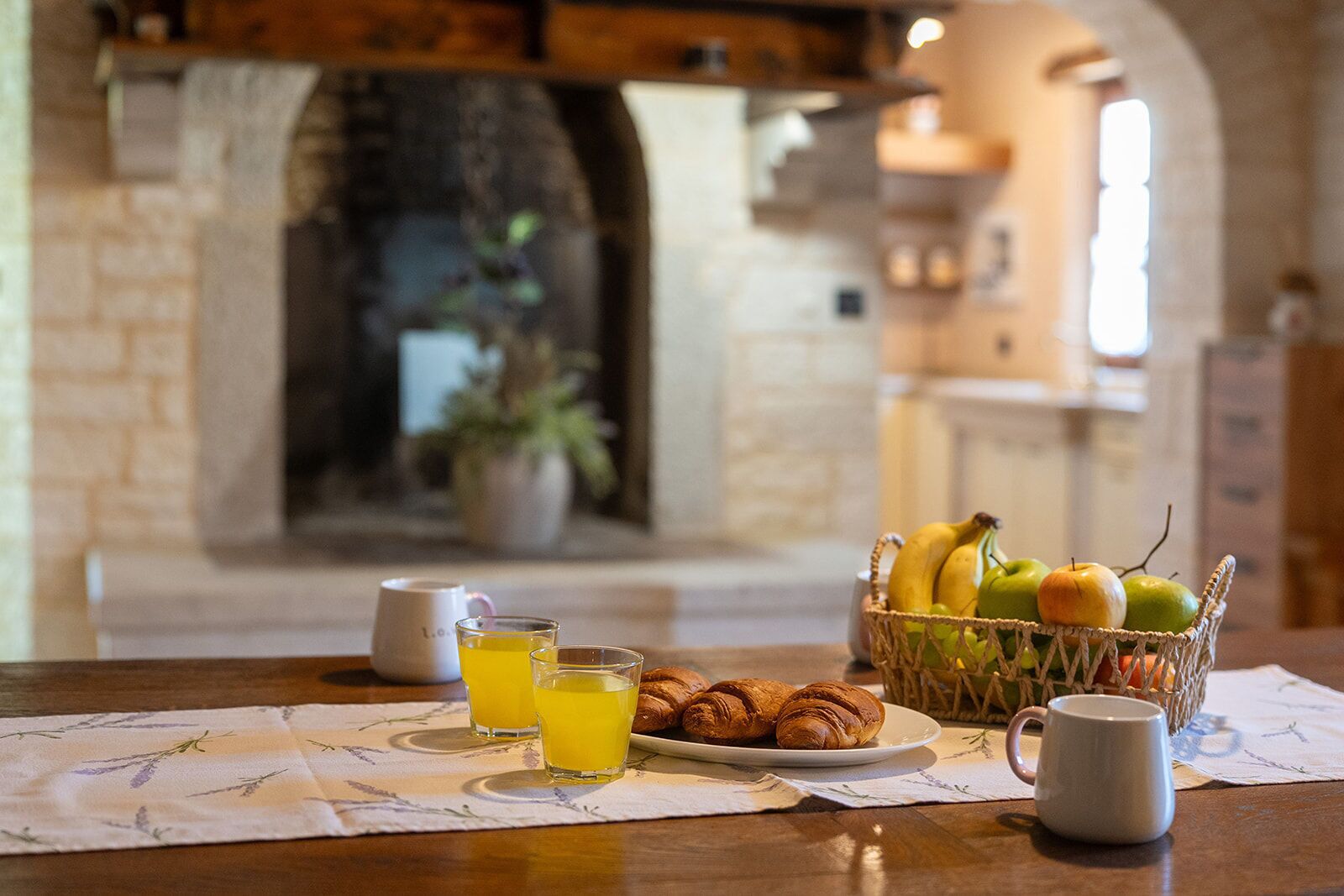 Un desayuno con una cesta de frutas, cruasanes y una taza sobre una mesa.