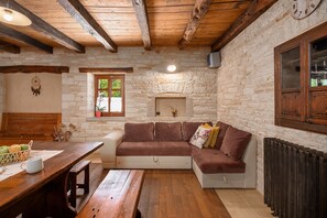 Ein rustikales Steinzimmer mit Holzbalkendecke, einem Steinkamin, einem Holztisch mit Korb und einem braunen Sofa.