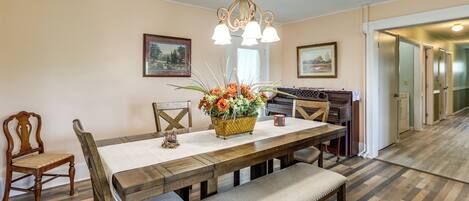 A dining area with a wooden table, chairs, a bench, a chandelier, and a vase of flowers.