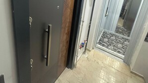 A hallway with a dark door, a tiled floor, and a visible pipe running along the wall. - Luxury 2+1 Apartment, 1st Floor – 15 Minutes to the Airport (Arnavutköy)