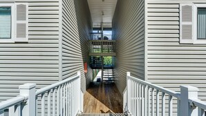 Un couloir doté d’un plancher en bois et de rampes blanches, qui mène à un balcon offrant une vue sur la verdure.