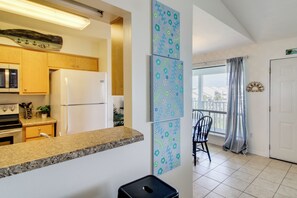 Eine Küche mit Kühlschrank, Mikrowelle und Holzschränken. Zwei gerahmte Kunstwerke sind an der Wand zu sehen.