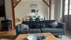 Ein Wohnzimmer mit grauem Sofa, einem Holztisch, einem roten Herd und einem Essbereich im Hintergrund.