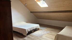 Ein Schlafzimmer mit schrägem Dach, einem Bett, einem Nachttisch und einem kleinen Fenster.