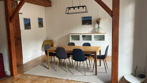 Ein Essbereich mit einem Holztisch, blauen Stühlen, einer hängenden Leuchte und einem weißen Schrank mit Glastüren.