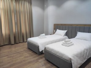 Hotellihuone, jossa on kaksi sänkyä, puulattia ja suuri ikkuna, jossa on verhot.