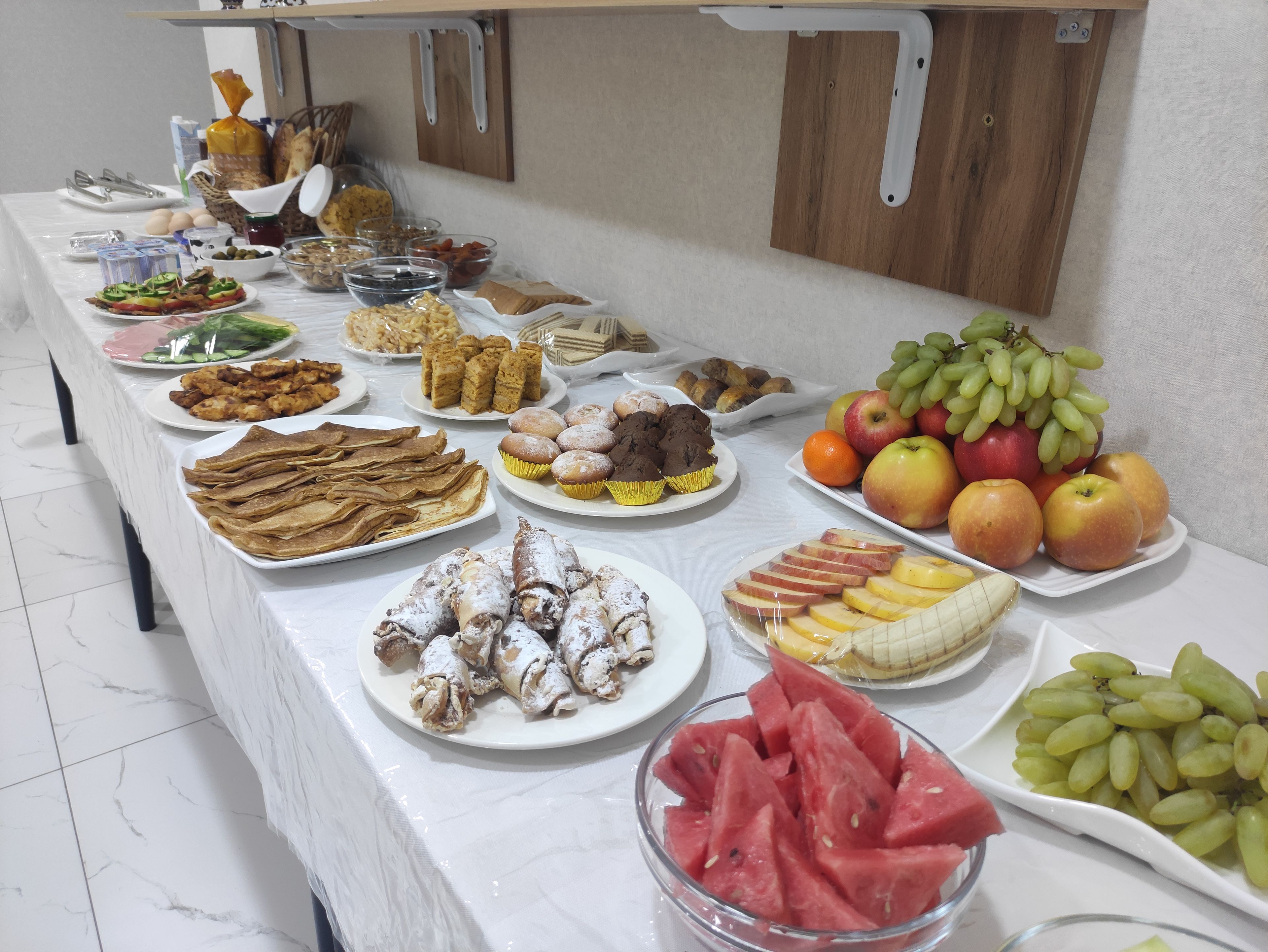 Une table de buffet proposant une variété d’aliments, notamment des fruits, des pâtisseries et des sandwichs.