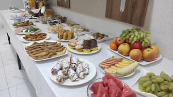 Une table de buffet proposant une variété d’aliments, notamment des fruits, des pâtisseries et des sandwichs.