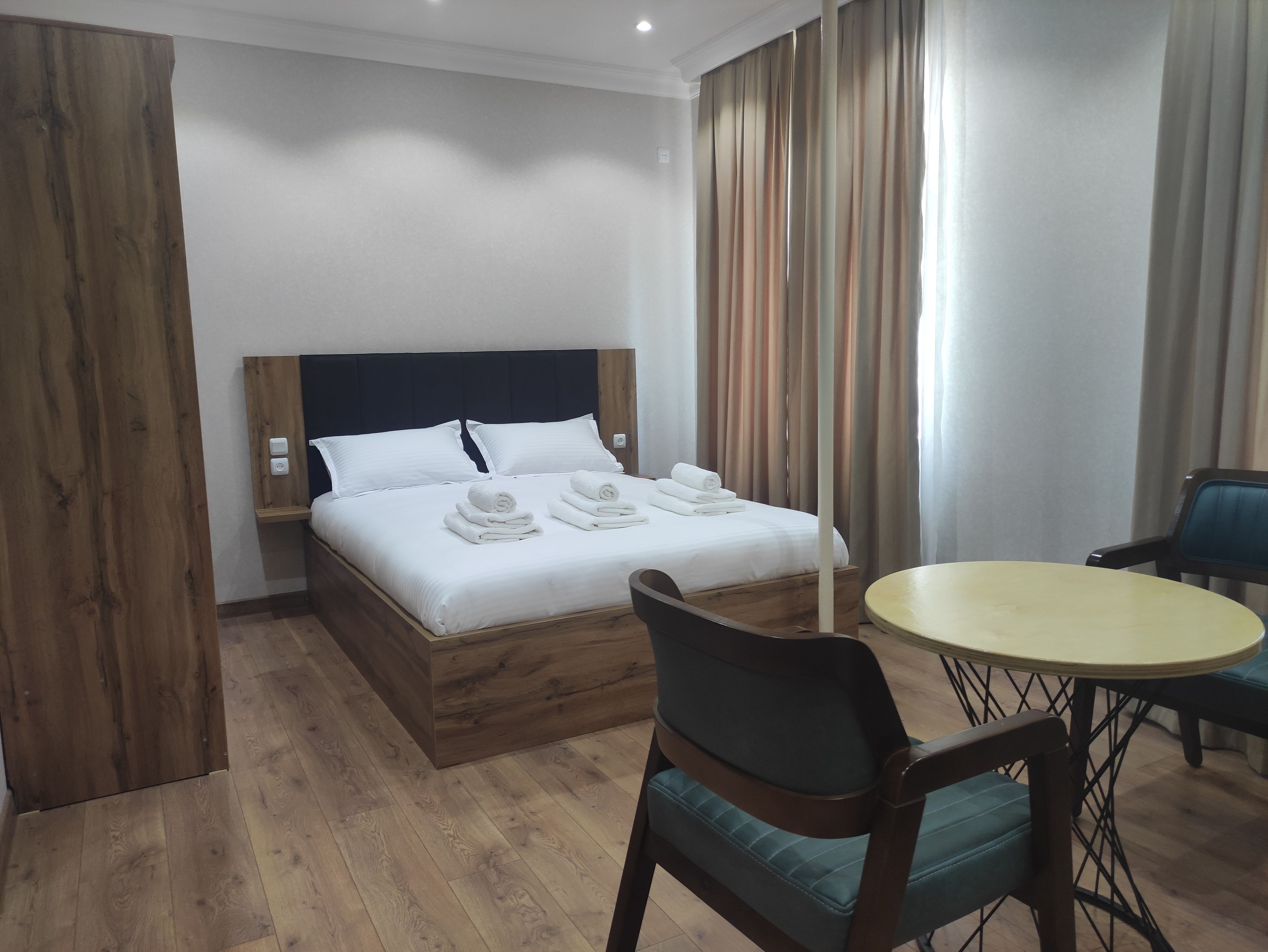 Ein Hotelzimmer mit einem Bett, einem Nachttisch, einem Sessel, einem runden Tisch und einem Vorhang.