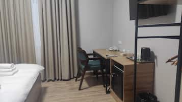 Ein Hotelzimmer mit Bett, Schreibtisch, Stuhl, Kaffeemaschine und Mülleimer.