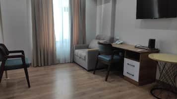 Ein modernes Zimmer mit Holzboden, einem grauen Sofa, einem Schreibtisch mit Stuhl, einem an der Wand befestigten Fernseher und einer Klimaanlage.