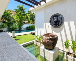 A pool area with a stone sculpture, a white wall, and a pergola. - The Wangsa Hotel and Villas (Nusa Dua)