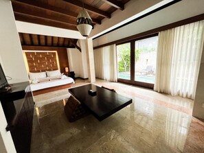 Ein geräumiges Zimmer mit großem Fenster, einem Bett, einem Esstisch und einem Deckenventilator.