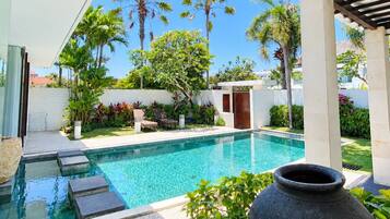 Una piscina con una pérgola, rodeada de exuberante vegetación y un cielo azul despejado.