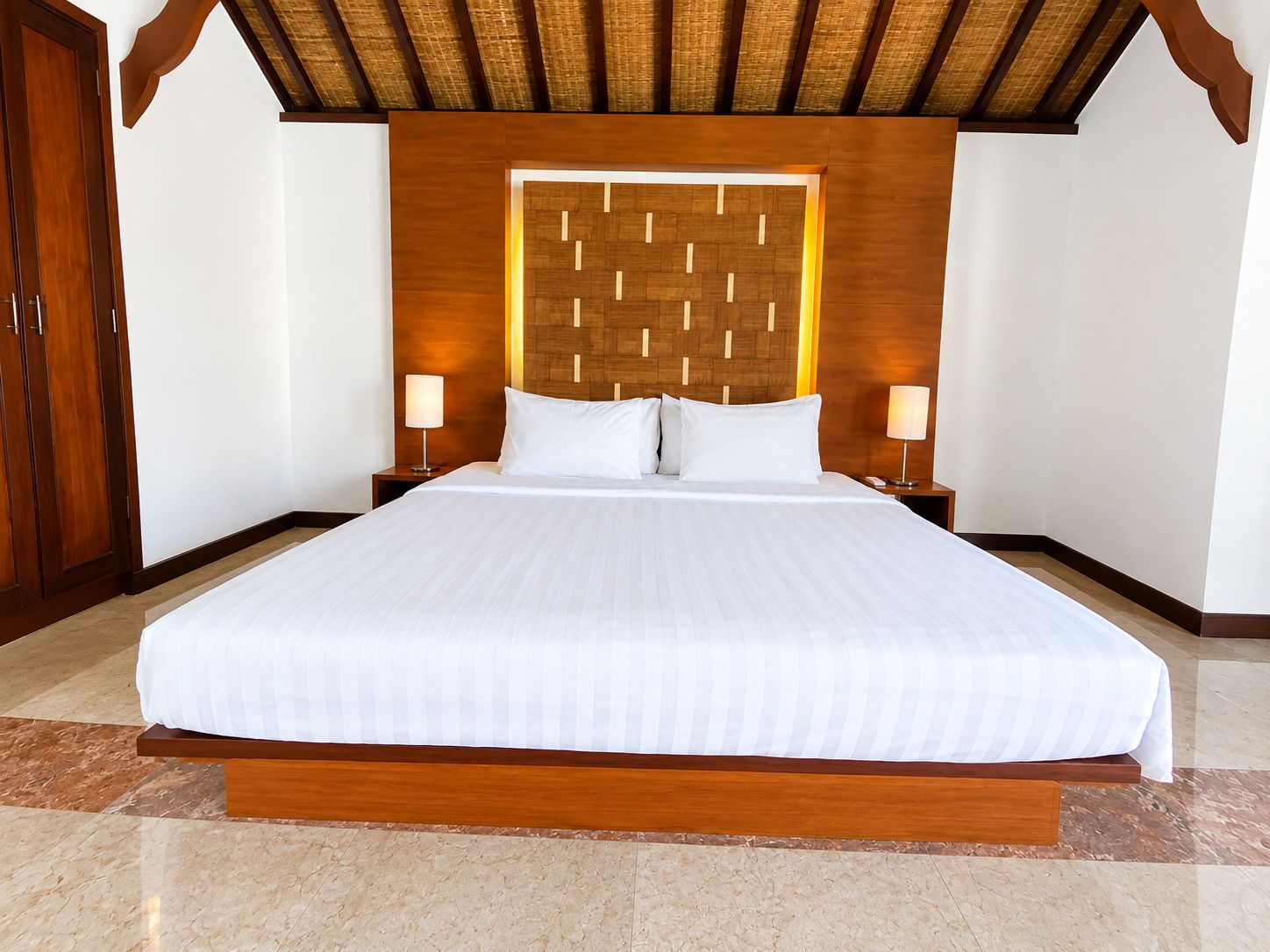 A large bed with a wooden headboard, two bedside lamps, and a wooden wardrobe.