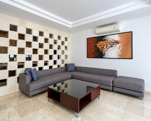 A modern living room with a sectional sofa, a glass coffee table, and a geometric wall design. - The Wangsa Hotel and Villas (Nusa Dua)