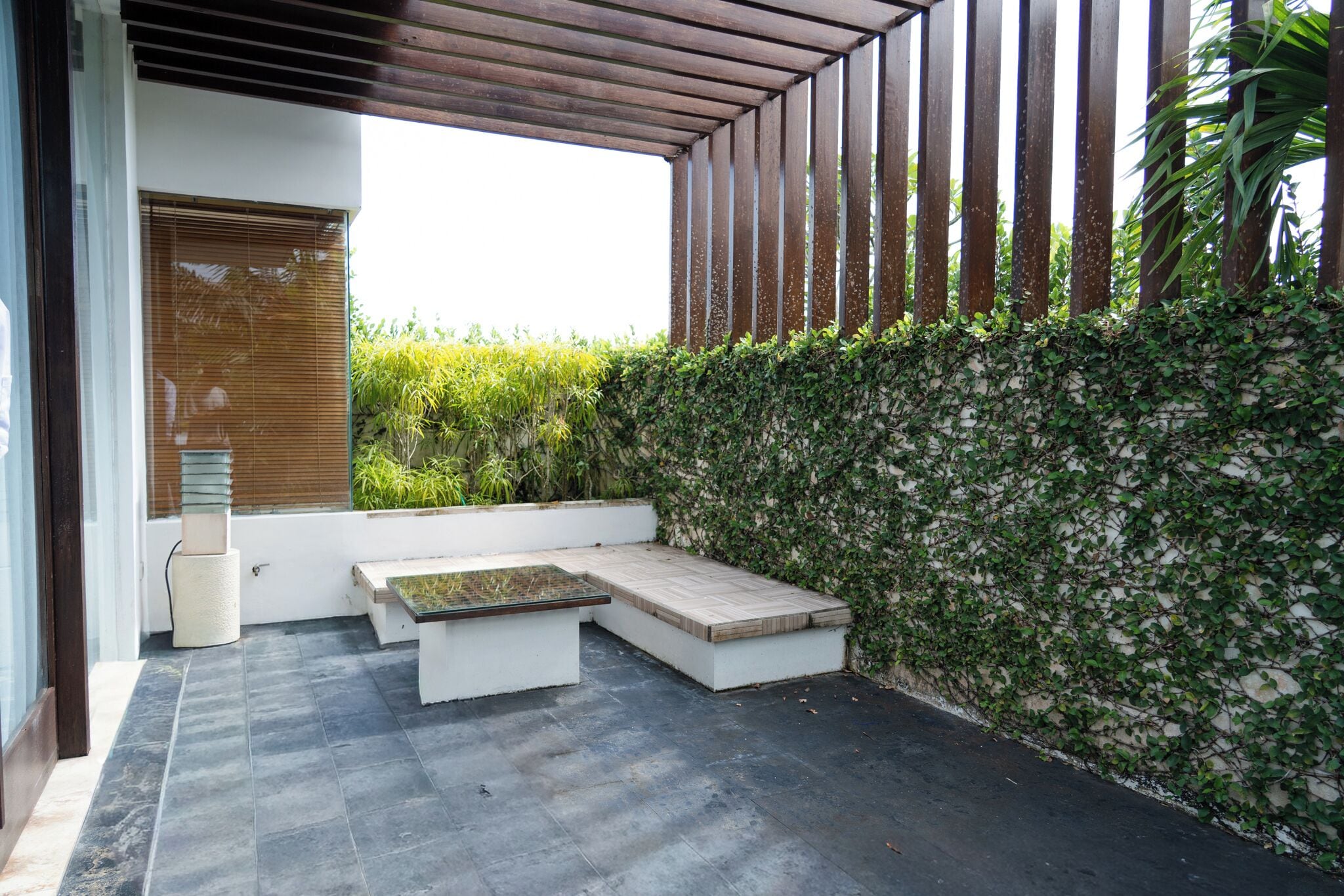 Een terras met een bank en tafel, omringd door een muur met klimplanten.