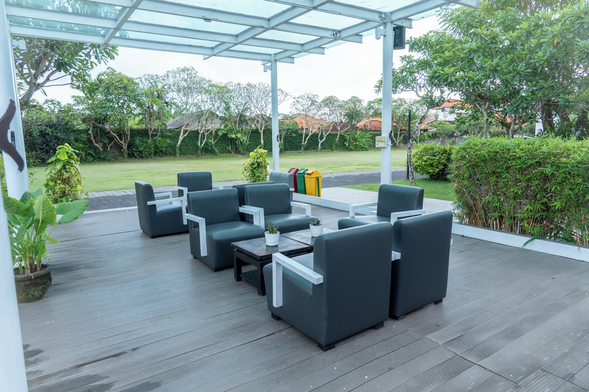 An outdoor patio with a covered seating area, a trash bin, and a garden in the background.