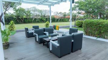 An outdoor patio with a covered seating area, a trash bin, and a garden in the background.