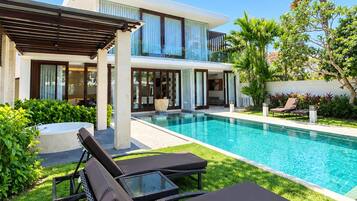 Una casa moderna con piscina, sillas de descanso y un patio cubierto.
