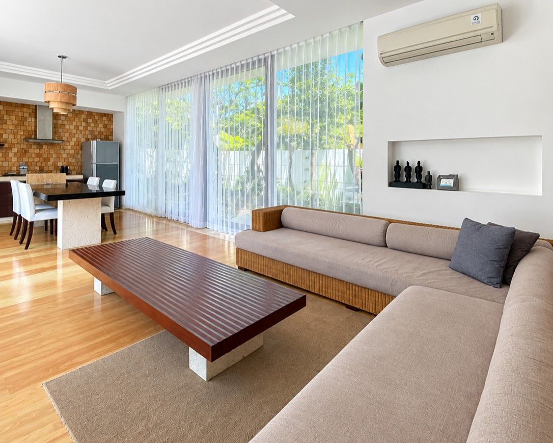A modern living room with a sofa, a wooden coffee table, and a dining area with a kitchen in the background.