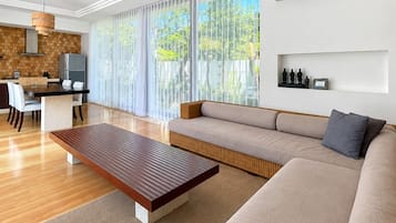 A modern living room with a sofa, a wooden coffee table, and a dining area with a kitchen in the background.