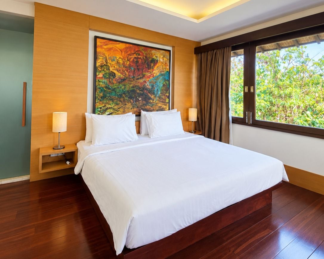 Una habitación de hotel con una cama grande, una mesita de noche, un cuadro en la pared y una ventana con cortinas.