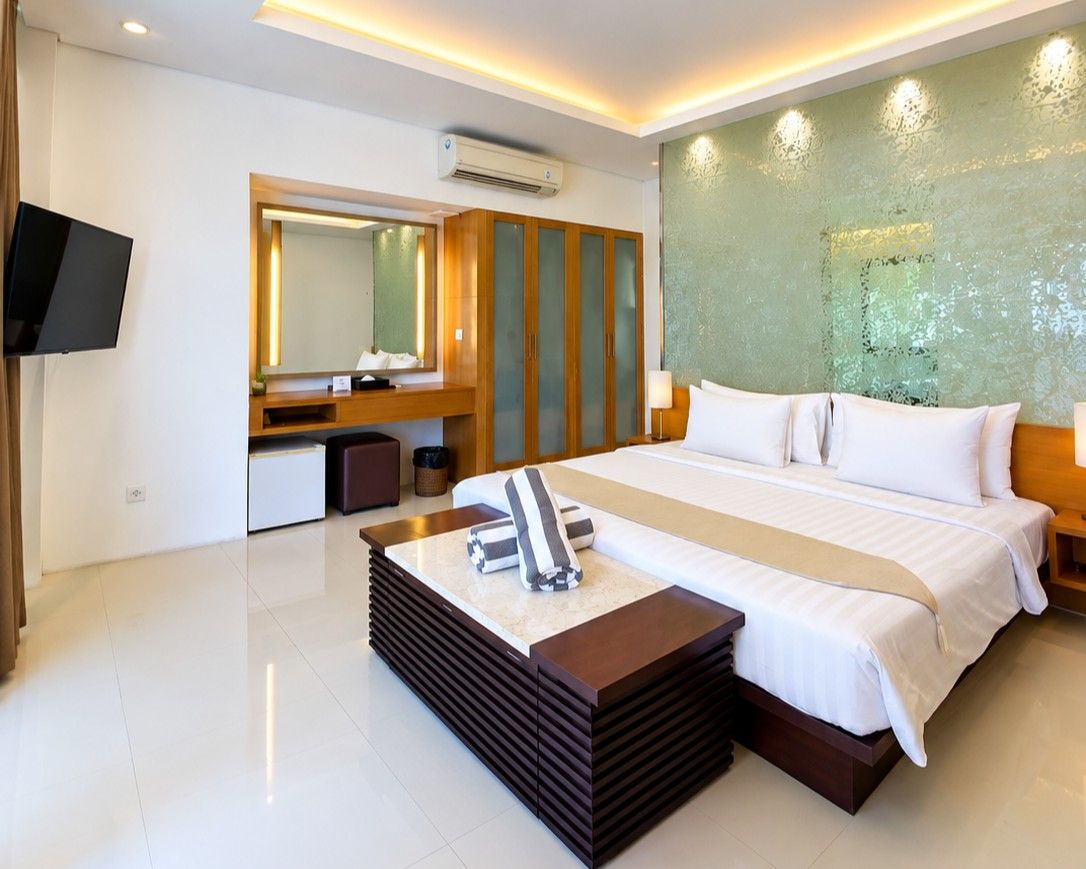 Habitación de hotel con una cama grande, una mesita de noche, un espejo, un televisor y un aire acondicionado instalado en la pared.
