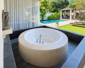 A circular bathtub in a modern bathroom with a view of a pool and garden. - The Wangsa Hotel and Villas (Nusa Dua)