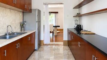A modern kitchen with wooden cabinets, a stainless steel refrigerator, a sink, and a countertop with a blender.