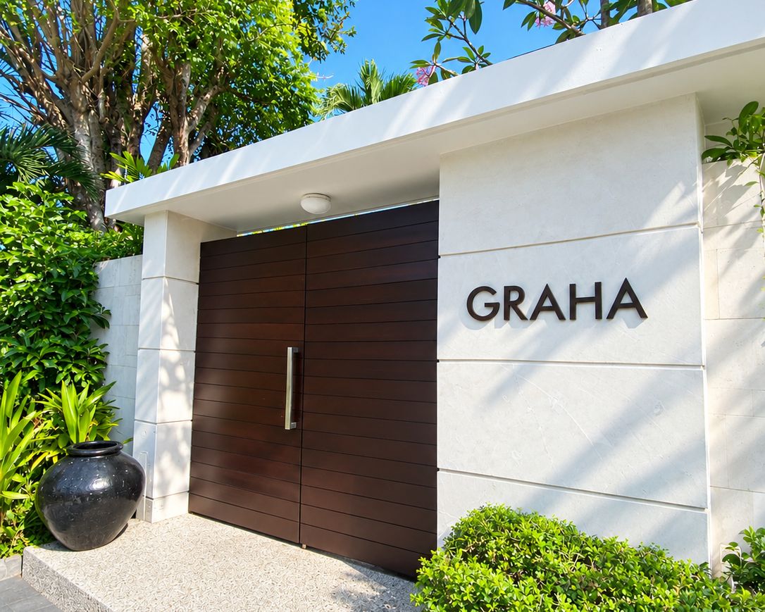 Entrada de un edificio moderno con una puerta de madera oscura y el nombre 'GRAHA' en la pared.