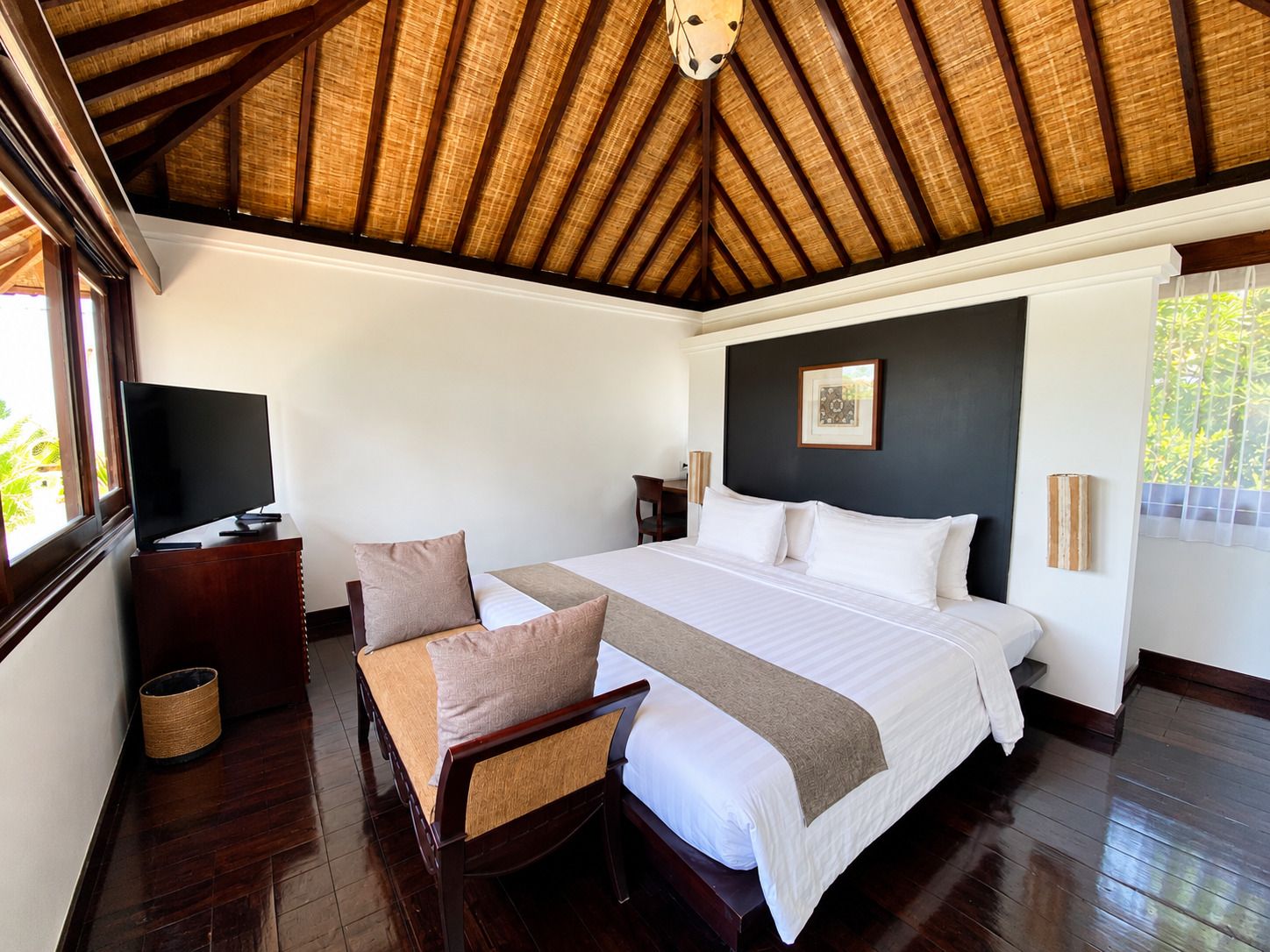 A hotel room with a large bed, a desk, a chair, a television, and a ceiling with wooden beams.