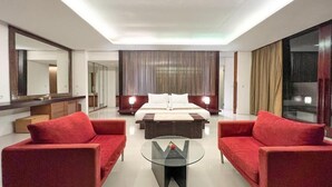 Una habitación de hotel moderna con una cama grande, dos sofás rojos, una mesa de centro de cristal y un espejo amplio.