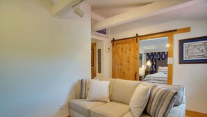 Una sala de estar con un sofá color beige, almohadones estampados, una puerta corredera con marco de madera y una obra de arte náutica enmarcada en la pared.