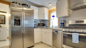 Una cocina moderna con electrodomésticos de acero inoxidable, armarios blancos y piso de baldosas.