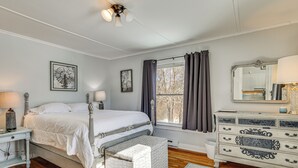 Une chambre à coucher comprenant un lit, des tables de chevet, une commode, une fenêtre avec des rideaux et des œuvres d’art accrochées aux murs.