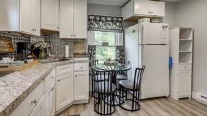 Une cuisine avec des meubles blancs, un plan de travail en marbre, une table en verre et des chaises noires.