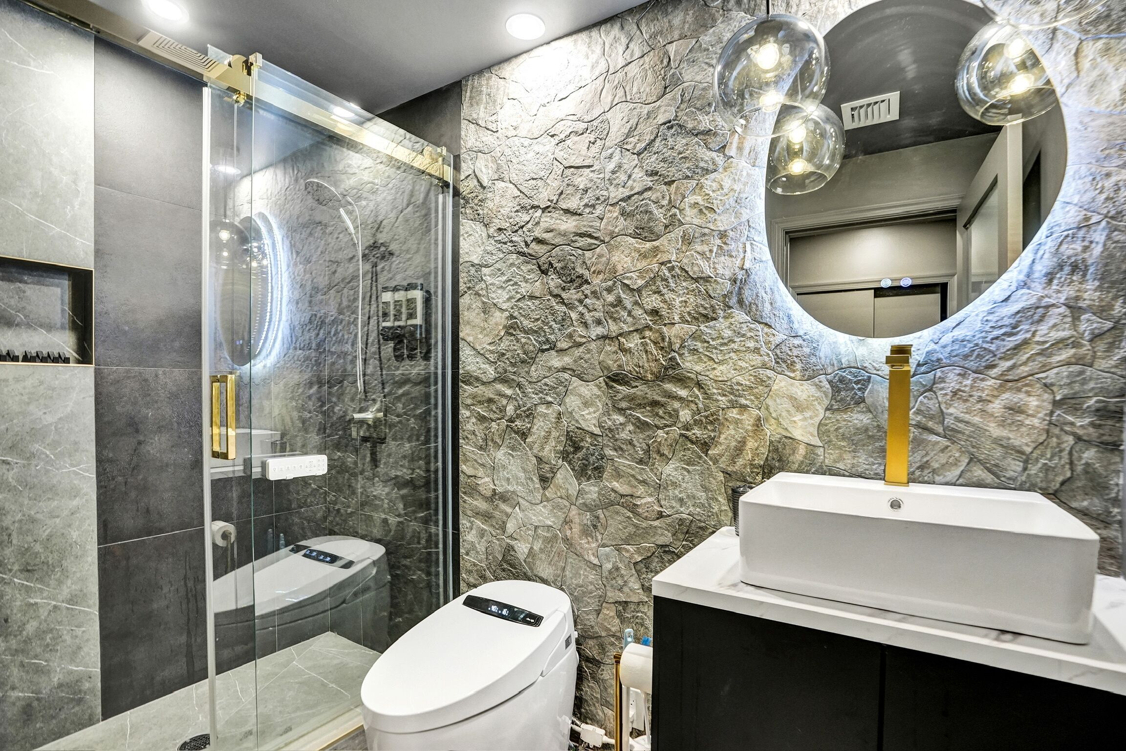 A modern bathroom with a glass-enclosed shower, a white sink, and a stone-textured wall.