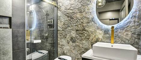 A modern bathroom with a glass-enclosed shower, a white sink, and a stone-textured wall.