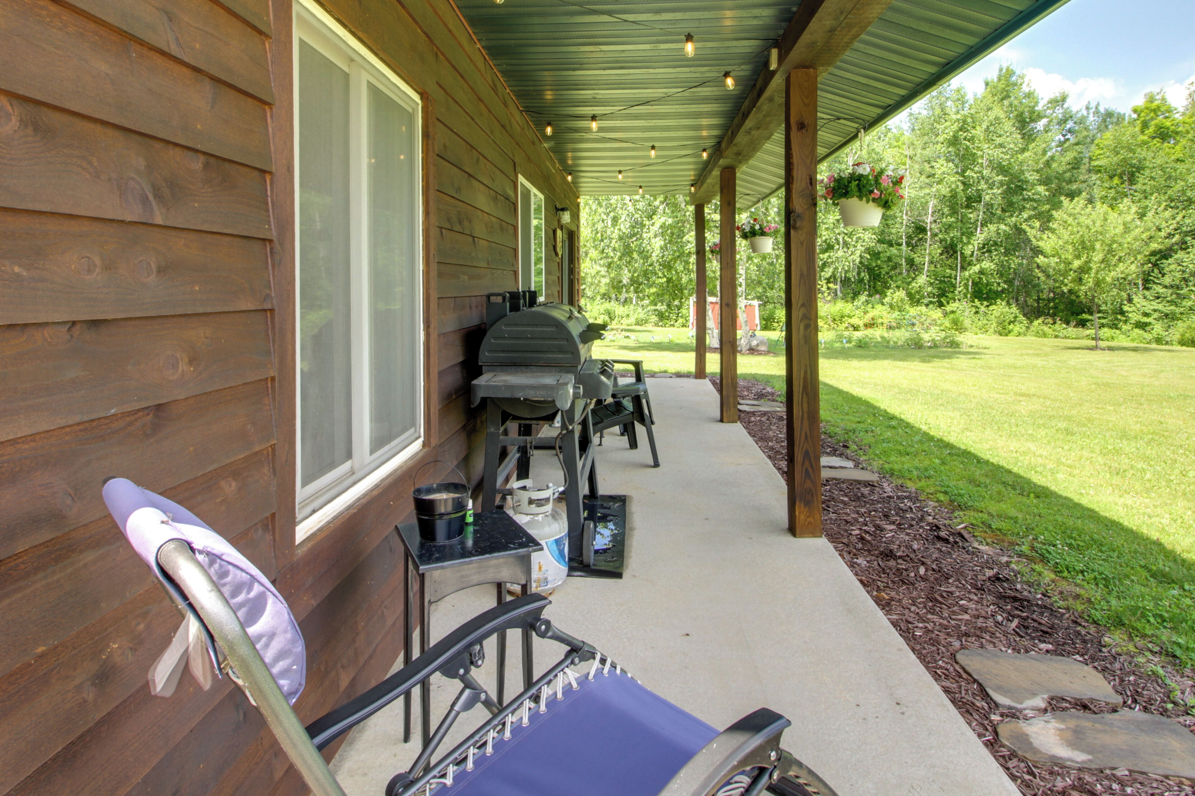 A covered porch with a grill, outdoor seating, and a hanging planter.