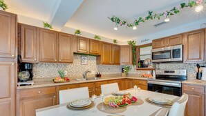 A modern kitchen with wooden cabinets, a stainless steel microwave, and a dining table set for a meal. - Group-Ready Oasis w/ Pool & Games in Port Richey (Port Richey)